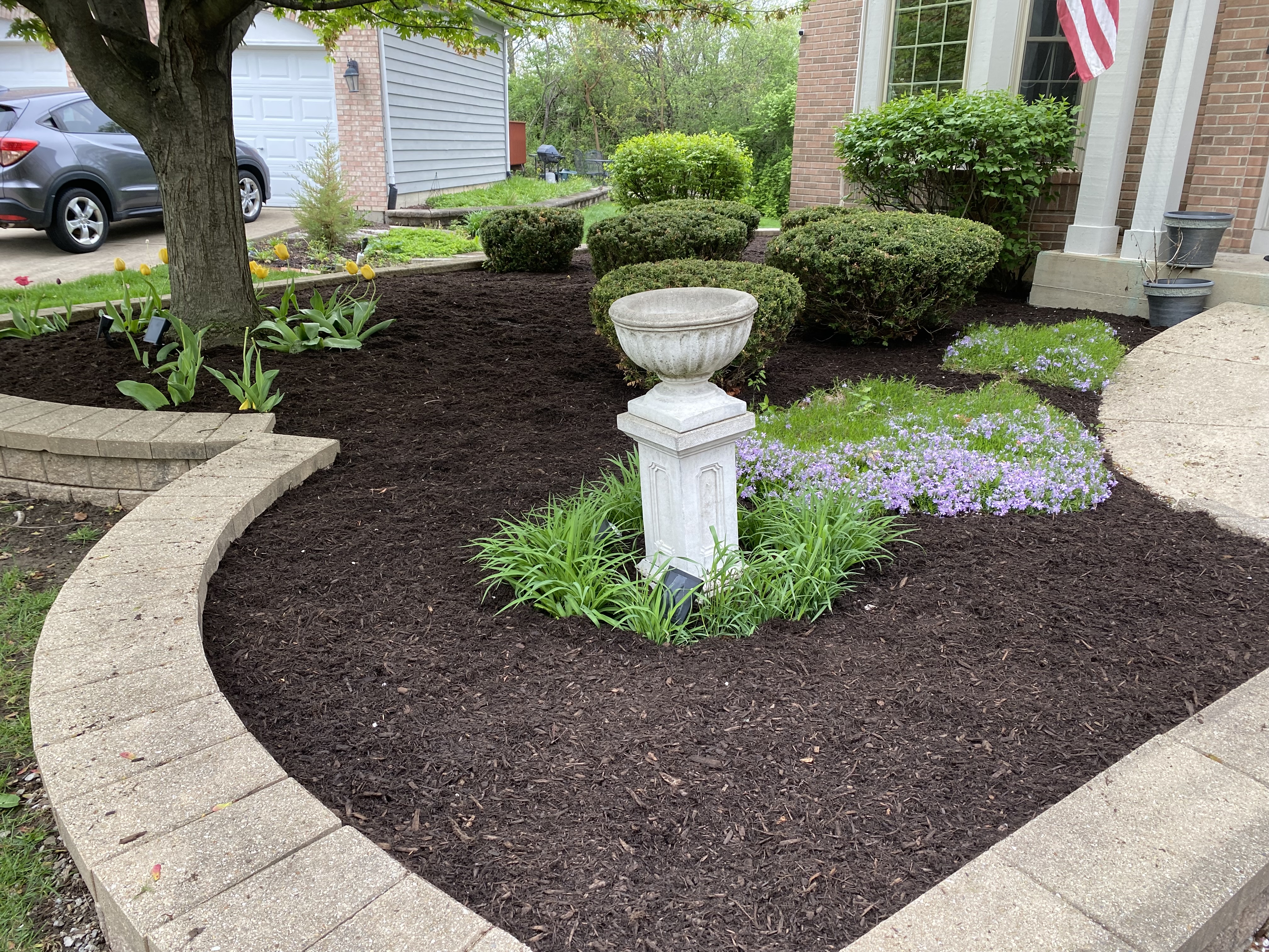 Curved front yard bed with dark mulch and stone edging